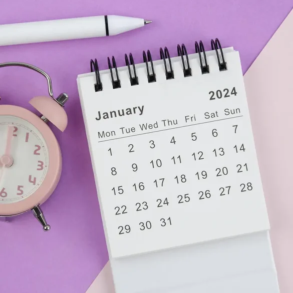 Calendario de enero de 2024 junto a un reloj despertador rosa y un bolígrafo sobre fondo en tonos pastel, representando la percepción prolongada del primer mes del año.