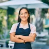 Mujer emprendedora con delantal sonriendo en un café al aire libre, simbolizando el acceso a oportunidades financieras.