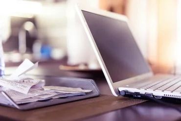 Computadora portátil encendida junto a una bandeja con recibos y facturas en una oficina, simbolizando el trabajo contable y fiscal que realizan los profesionales para cumplir con las obligaciones del SAT y evitar sanciones en las MiPyMEs mexicanas.
