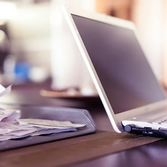 Computadora portátil encendida junto a una bandeja con recibos y facturas en una oficina, simbolizando el trabajo contable y fiscal que realizan los profesionales para cumplir con las obligaciones del SAT y evitar sanciones en las MiPyMEs mexicanas.