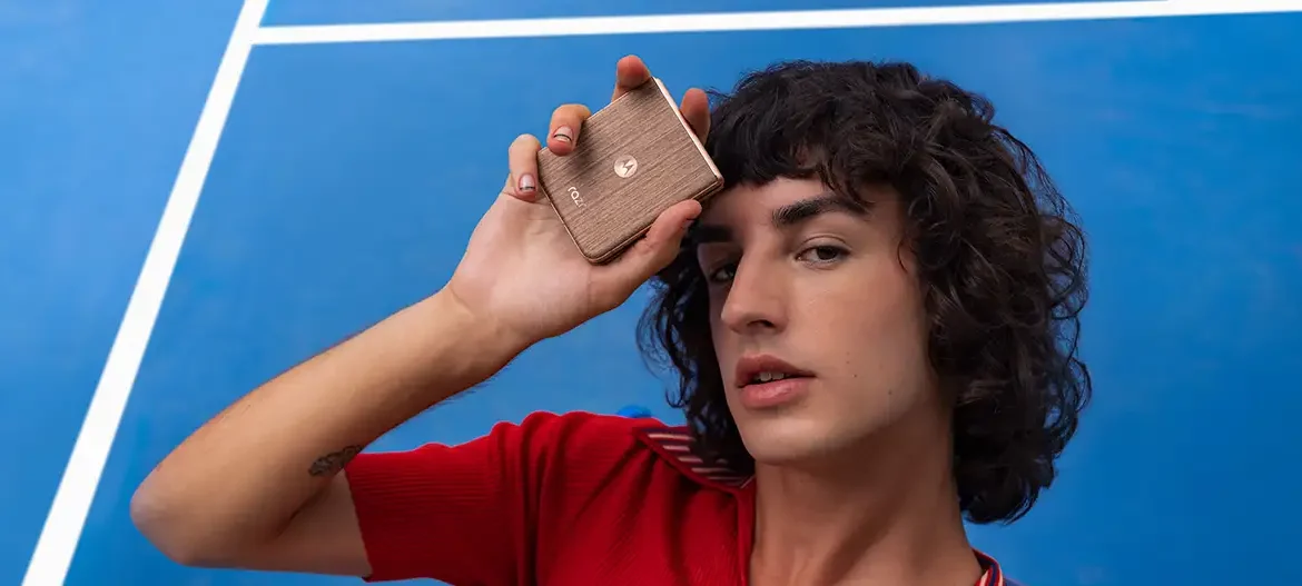 Persona sostiene un smartphone Motorola razr 60 ultra en tono dorado mientras posa frente a una cancha azul, destacando el diseño compacto y elegante del dispositivo plegable.