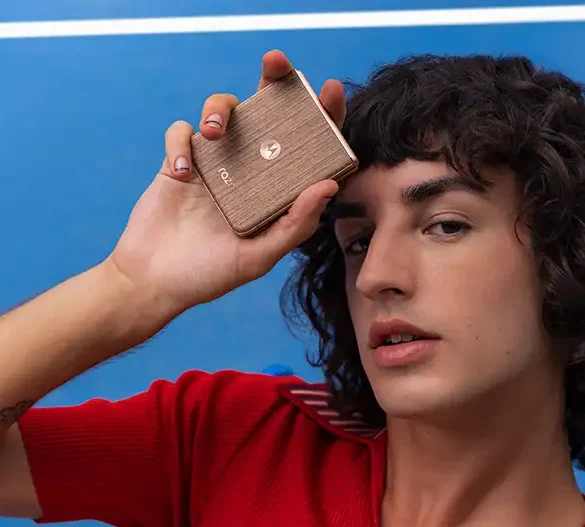 Persona sostiene un smartphone Motorola razr 60 ultra en tono dorado mientras posa frente a una cancha azul, destacando el diseño compacto y elegante del dispositivo plegable.