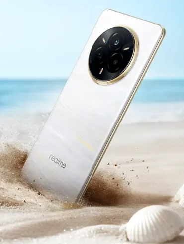 El realme 14 Pro, con diseño perlado y módulo de cámara circular, se muestra parcialmente enterrado en la arena de una playa, destacando su resistencia IP69 al polvo y agua, ideal para estilos de vida activos y fotografía en exteriores