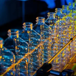 Línea de producción de botellas plásticas iluminada con luces industriales durante el proceso de fabricación automatizada.