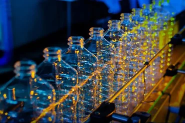 Línea de producción de botellas plásticas iluminada con luces industriales durante el proceso de fabricación automatizada.