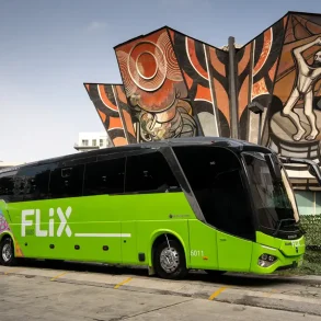 Autobús verde de Flix estacionado frente al emblemático mural del Polyforum Cultural Siqueiros en Ciudad de México, marcando el inicio de operaciones de la empresa alemana en el país.