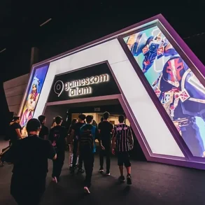 Entrada principal de gamescom latam 2025 en São Paulo, con asistentes ingresando al recinto bajo una estructura iluminada y pantallas LED con arte de videojuegos.