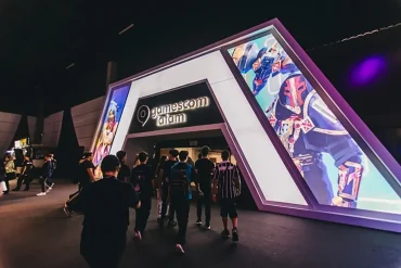 Entrada principal de gamescom latam 2025 en São Paulo, con asistentes ingresando al recinto bajo una estructura iluminada y pantallas LED con arte de videojuegos.