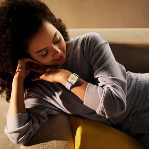 Mujer recostada observando su smartwatch HUAWEI WATCH FIT 4 en tono lavanda, destacando su diseño elegante y funciones de monitoreo de salud.