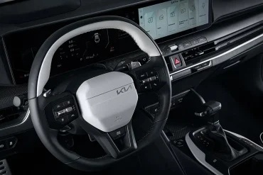Volante del Kia K4 2025 con diseño bicolor, controles multifunción integrados y pantalla digital panorámica al fondo, destacando la experiencia de usuario intuitiva reconocida por Wards como una de las mejores del año.