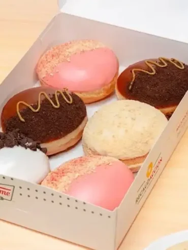 Caja de donas edición limitada de Krispy Kreme inspiradas en sabores de cheesecake, con coberturas de fresa, chocolate, galleta y cookies & cream.