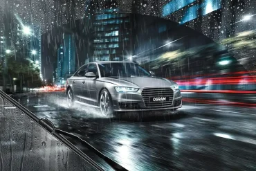 Automóvil sedán circulando bajo la lluvia con limpiaparabrisas OSRAM en acción, mostrando una visibilidad óptima en condiciones climáticas adversas.