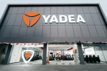 Fachada de una tienda Yadea con logo iluminado y exhibición de scooters eléctricos en su interior.