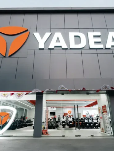 Fachada de una tienda Yadea con logo iluminado y exhibición de scooters eléctricos en su interior.
