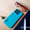 Smartphone HONOR X8c en color azul sobre escritorio de madera, acompañado de lentes, libreta negra, bolígrafo blanco y clip metálico.