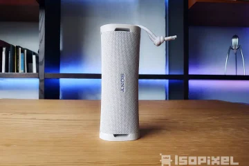 Bocina portátil Sony ULT Field 1 en color blanco, colocada en posición vertical sobre una mesa de madera, con fondo iluminado en tonos azules y morados, ideal para interiores modernos. Destaca su diseño compacto, textura de malla y correa ajustable.
