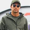 Checo Pérez camina por el paddock de la Fórmula 1 con gafas oscuras, gorra y chaqueta verde, previo al posible anuncio con Cadillac F1 en 2026.
