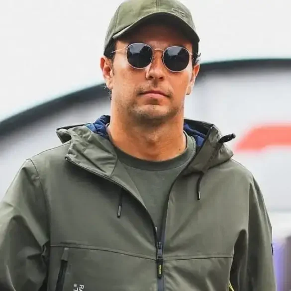 Checo Pérez camina por el paddock de la Fórmula 1 con gafas oscuras, gorra y chaqueta verde, previo al posible anuncio con Cadillac F1 en 2026.