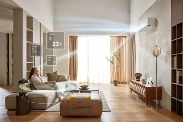 Mujer relajada en una sala moderna con aire acondicionado LG DUALCOOL funcionando a 23 °C. La interfaz holográfica muestra dirección, velocidad y temperatura del aire, destacando la tecnología inteligente y personalizable del sistema de climatización.