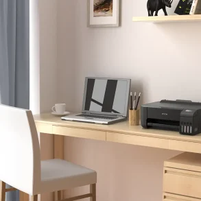 Espacio de trabajo en casa con una impresora Epson EcoTank L1250 sobre un escritorio de madera clara junto a una laptop y botellas de tinta de repuesto.