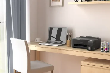 Espacio de trabajo en casa con una impresora Epson EcoTank L1250 sobre un escritorio de madera clara junto a una laptop y botellas de tinta de repuesto.