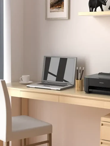 Espacio de trabajo en casa con una impresora Epson EcoTank L1250 sobre un escritorio de madera clara junto a una laptop y botellas de tinta de repuesto.