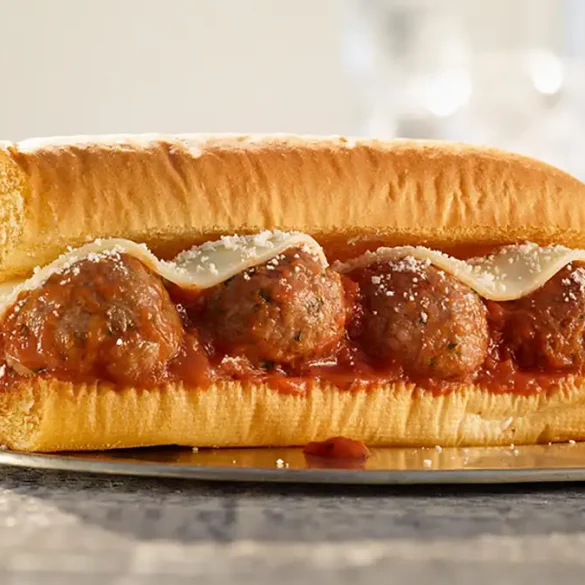 Primer plano de un Sub de Albóndigas de Subway servido en pan recién horneado, con albóndigas de res cubiertas de salsa marinara, queso mozzarella derretido y un toque de parmesano rallado, capturado sobre una superficie de madera con iluminación natural.