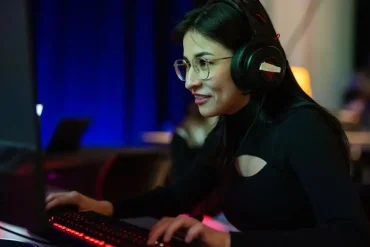 Estudiante concentrada juega en computadora con auriculares en un programa educativo basado en videojuegos.