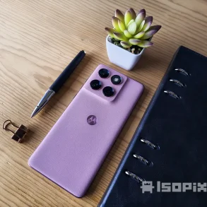 Smartphone Motorola rosa con cuatro cámaras traseras sobre mesa de madera, acompañado de pluma, clip dorado, libreta negra y maceta decorativa.