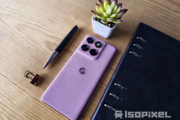 Smartphone Motorola rosa con cuatro cámaras traseras sobre mesa de madera, acompañado de pluma, clip dorado, libreta negra y maceta decorativa.