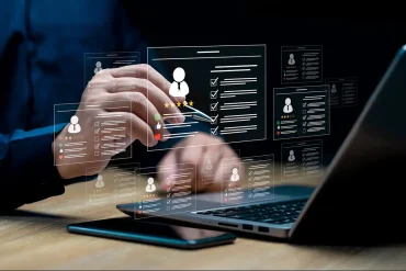 Manos interactúan con una interfaz digital de reclutamiento impulsada por inteligencia artificial, mostrando perfiles y evaluaciones de candidatos.