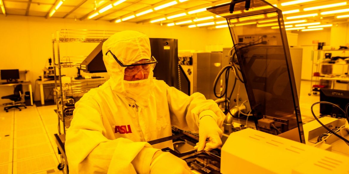 Investigador de Arizona State University manipula obleas de silicio en un laboratorio de semiconductores equipado con iluminación amarilla controlada.