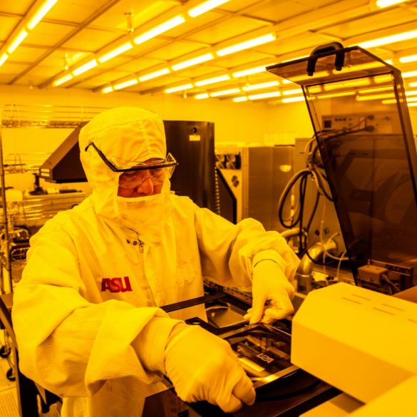 Investigador de Arizona State University manipula obleas de silicio en un laboratorio de semiconductores equipado con iluminación amarilla controlada.