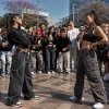 Dos mujeres compiten en una batalla de farmear aura mientras una multitud las rodea y graba con sus smartphones.