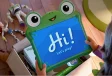 Niña sostiene tablet interactiva de rana con mensaje “Hi! Let’s play!” junto a juguetes de Toy Story en el suelo